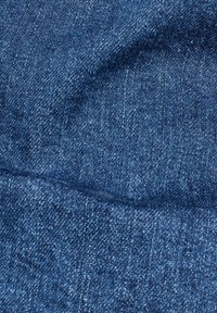 Närbild av blå denimtyg som visar detaljerad vävstruktur och en synlig sömspricka.