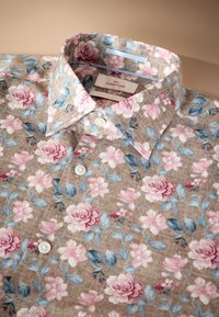 Bloemenoverhemd in beige stof met roze en blauwe bloemen, voorzien van een klassieke kraag en witte knopen, gedetailleerd met een gestructureerd patroon.