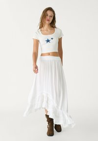 Hvid crop top med blå stjernebroderi, parret med en flydende hvid maxiskirt med blondedetail og brune ankelstøvler.
