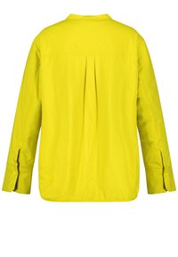 Žlutá lehká bunda s zadním skladem, dlouhými rukávy a bočními otvory. Hladká textura a neformální design vhodný pro různé příležitosti.
