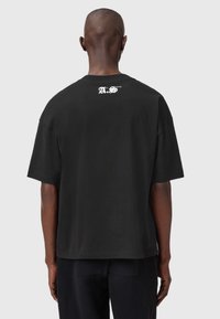 Must reisi lühikeste varrukatega must puuvillane T-särk, millel on mugav lõige. Ülaseljal on valge logo. Sile tekstuur, klassikaline ümmargune kaelus.
