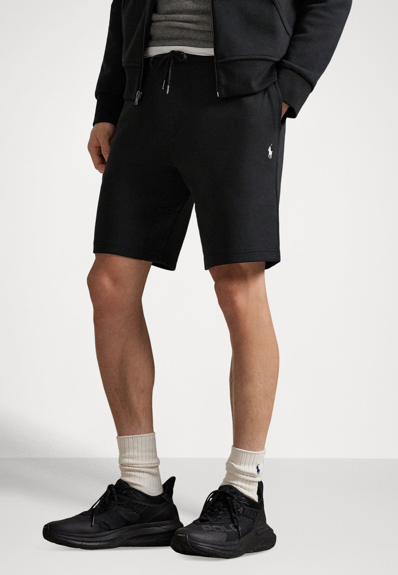 Black athletic shorts made of a soft fabric with an elastic waistband and drawstring. Features a small white logo on the left leg.