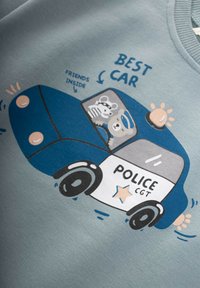 Grafika zobrazuje svetlomodré mikinu s cartoon policajným autom. Auto je modré s bielou stranou, vo vnútri sú cartoon zvieratá a dekoratívny text.