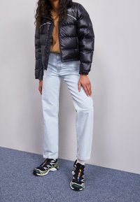 Black puffer jacket with horizontal quilted pattern, light blue straight-leg jeans, and black athletic shoes with colorful accents.