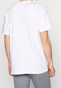 Vit bomulls-T-shirt med korta ärmar och rundad halsringning. Slät textur och avslappnad passform. Etikett synlig på vänster ärm.