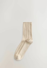 Chaussette beige tricotée jusqu'au milieu du mollet avec un motif côtelé et des rayures verticales texturées, posée à plat sur un fond clair.