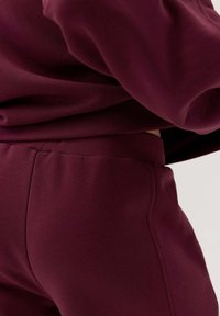 Bordowy sweatshirt i pasujące dresowe spodnie wykonane z miękkiej mieszanki bawełny, z elastyczną talią i mankietami, charakteryzujące się gładką teksturą.