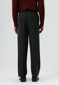 Donkergrijze broek met wijde pijpen van gestructureerde stof, voorzien van een enkele achterzak, een knoopsluiting en een geplooid ontwerp.