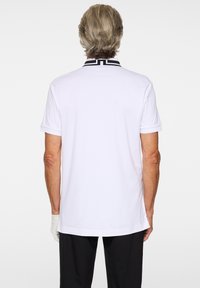 Biała koszulka polo z kontrastującym czarnym kołnierzem ozdobionym geometrycznym wzorem. Projekt obejmuje krótkie rękawy i prosty dół.