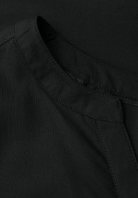 Tessuto nero con una consistenza liscia. Presenta un collo rotondo e dettagli cuciti. Include una cerniera nascosta sul lato.