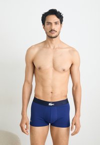 Marineblauwe boxershorts met een marineblauwe tailleband en een wit logo. Zachte stof, aansluitend ontwerp, lengte tot halverwege de dij, gladde textuur.