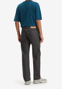 Camicia a maniche corte teal da uomo, jeans di denim grigi con taglio dritto, tasche posteriori visibili, etichetta in pelle e scarpe sportive grigie.