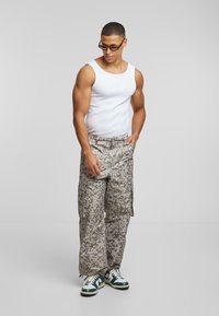 Cargo bukser i et lys gråt camouflage mønster, parret med en hvid tank top. Sneakers er sort og hvid med grønne accenter.