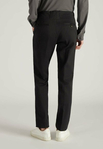 Pantaloni neri con design a gamba dritta, caratterizzati da una texture liscia, passanti per la cintura e due tasche posteriori. Abbinati a sneaker bianche.