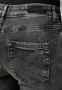 Jeans de denim gris con una textura desgastada, que cuentan con una etiqueta de cuero en la cinturilla y un bolsillo trasero único con costuras en contraste.