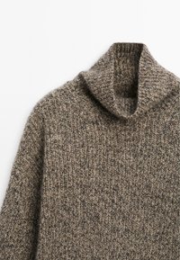 Maglione spesso a maglia in marrone e grigio con colletto a turtleneck piegato su sfondo bianco.