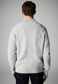 Grauer Strickpullover mit hochgeschlossenem Kragen, strukturiertem Muster und gerippten Bündchen, getragen von einer Person, die von hinten betrachtet wird.