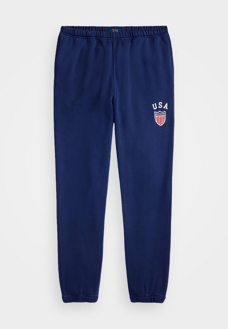 Pantalons de survêtement bleu marine avec taille élastique, chevilles resserrées et logo écusson "USA" brodé à l'avant. Texture de tissu douce et lisse.