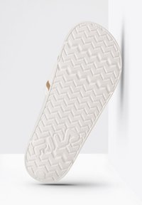 Semelle de sandale en caoutchouc blanc avec un motif en zigzag texturé, présentant une légère courbure et un logo estampé. Design minimaliste avec des bords lisses.