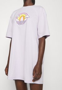 Ljuslila oversized t-shirt i bomull, med en färgglad grafisk design av en sol och moln på framsidan. Korta ärmar, avslappnad passform.