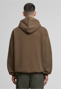 Brauner Kapuzenpullover mit entspannter Passform, überschnittenen Schultern und weichem Material. Die Rückansicht zeigt ein einfaches Design ohne Grafiken oder Logos.