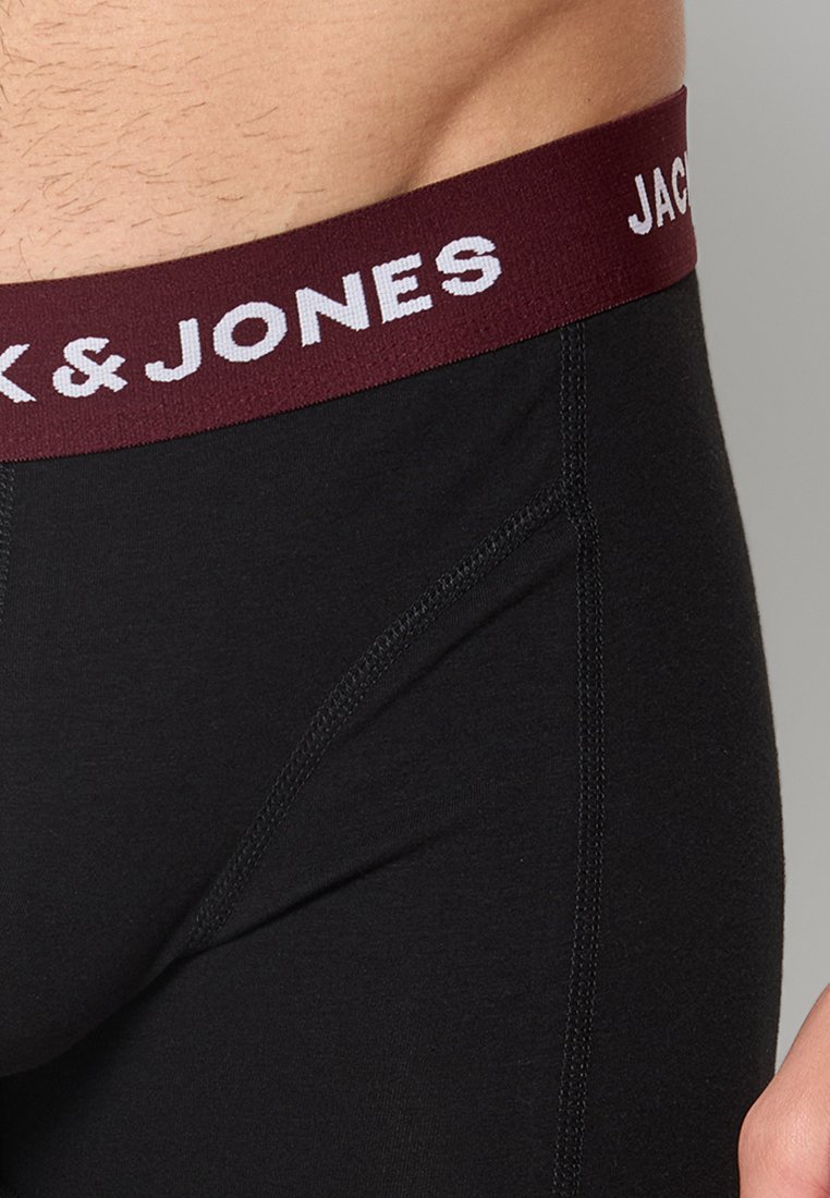 Primer plano de una persona que lleva calzoncillos negros con una cinturilla burdeos que muestra el texto blanco "JACK & JONES".