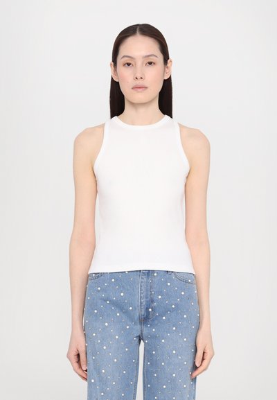 Haut sans manches blanc à col montant, associé à un jean en denim bleu avec des embellissements en studs argentés partout.