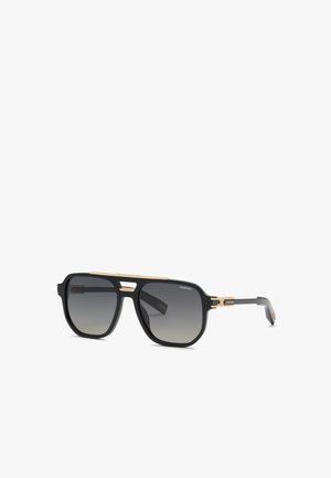 Lunettes de soleil aviateur noires et dorées avec verres foncés dégradés et détails fins dorés sur la monture et les branches, brandées avec le logo "Chopard".