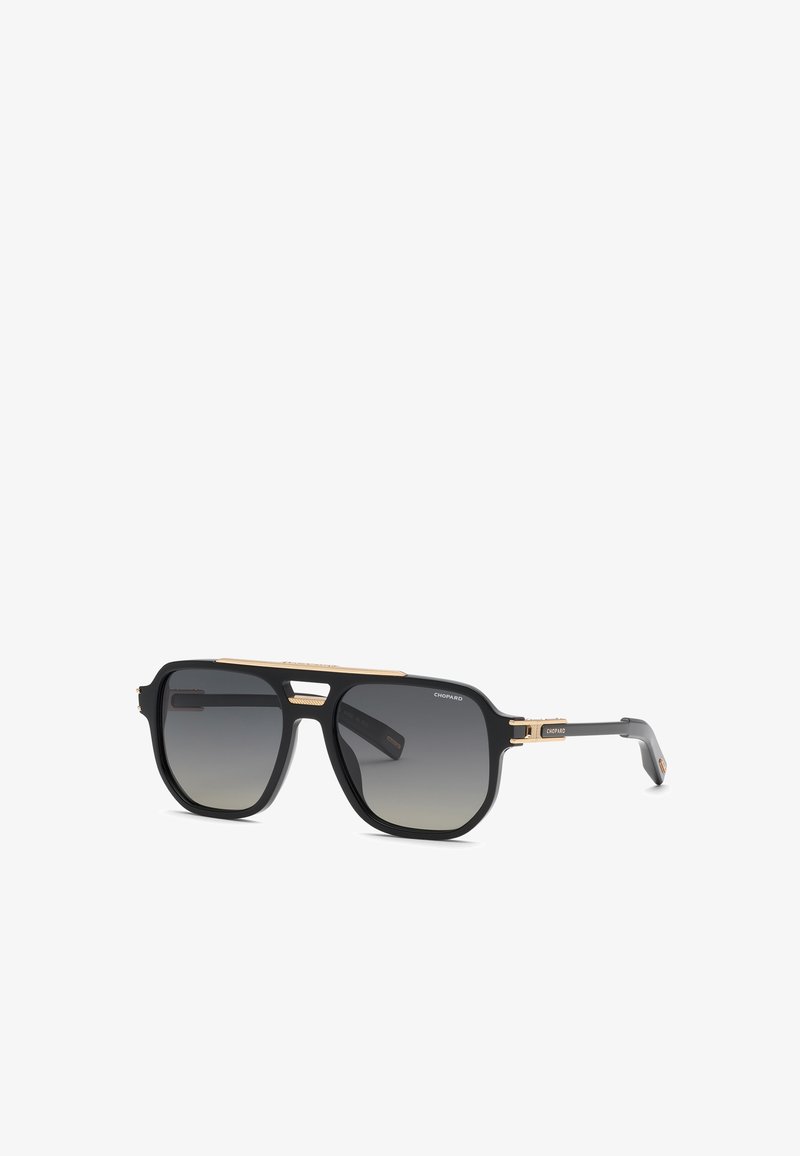 Lunettes de soleil aviateur noires et dorées avec verres foncés dégradés et détails fins dorés sur la monture et les branches, brandées avec le logo "Chopard".
