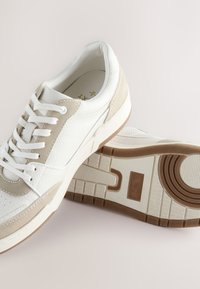 Hvide og beige sneakers med øverste del i struktureret læder og ruskind, rundet tå, snørelukning og gummisål med mønstret slidbane.