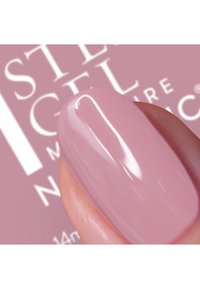 Ljust rosa gel-nagellack applicerad på ett finger, med en glansig yta. I bakgrunden är text relaterad till märket svagt synlig.