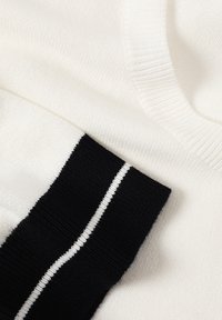 Pull en tricot blanc avec col côtelé et poignet noir orné d'une fine bande blanche sur la manche.