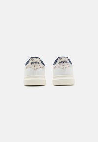 White sneakers with floral design and navy accents, featuring a textured heel and logo detail. Rubber sole, minimalist style.