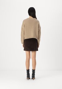 Pulover bej tricotat cu un design scurt și mâneci texturate, asortat cu o fustă din suede maro închis și cizme negre până la gleznă.