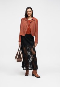 Καφέ μοτίβο cropped σακάκι πάνω από ένα τοπ σε σκουριά απόχρωση, συνδυασμένο με μαύρη δαντελένια φούστα, καφέ μπότες και καφέ τσάντα με λουράκι.