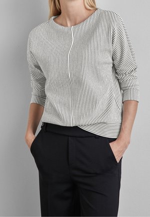Striped pullover in black and white, featuring a round neckline, three-quarter sleeves, and a relaxed fit. Paired with dark trousers.