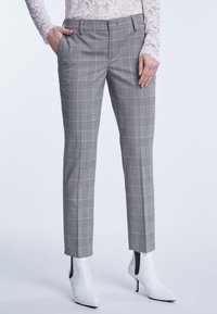 Grijze geblokte broeken met een tailored fit, voorzien van een vlakke voorkant, zijzakken en een gladde textuur. Gecombineerd met witte hoge enkellaarsjes.