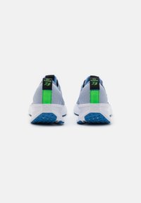 Zapatillas de running de malla grises con una suela blanca, con acentos verdes y negros en el talón y una suela externa azul texturizada.