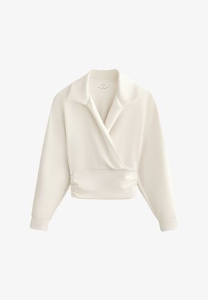 Krém színű hosszú ujjú átlapolt blúz széles gallérral, testhez simuló derékkal és mandzsettás ujjal, fehér háttéren bemutatva.