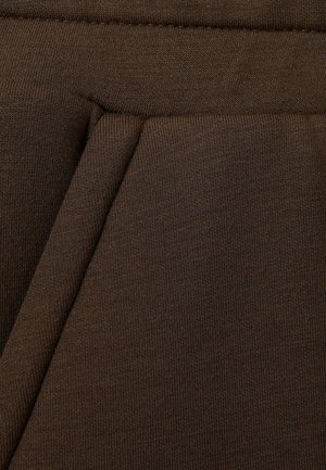 Tessuto marrone a coste con una finitura strutturata, caratterizzato da sezioni piegate che creano dimensione. Il materiale sembra elastico e morbido.