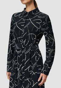 Abito blu navy con maniche lunghe e colletto, decorato con un motivo di cuori bianchi e scritte. Include una cintura in tessuto abbinata in vita.