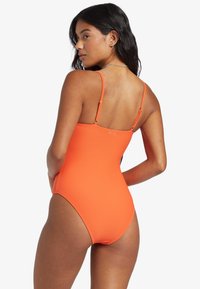 Maillot de bain une pièce orange à côtes avec des bretelles ajustables et une taille haute. Texture lisse et accents matériels minimaux.