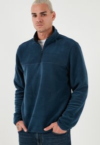 Pullover in pile blu navy con colletto a mezza zip e rifiniture nere a contrasto. Presenta maniche lunghe e una texture liscia e morbida.