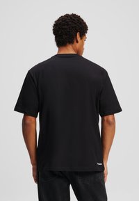 Zwarte t-shirt met korte mouwen, gemaakt van katoen, met een ronde hals en een rechte zoom. De achterkant toont een subtiele merkl logo nabij de zoom.