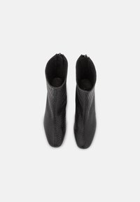 Bottines noires à la cheville avec un motif texturé tissé. Elles disposent d'une fermeture éclair et d'une silhouette élégante, fabriquées en simili cuir.