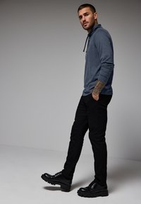 Camiseta de manga larga gris oscuro con capucha, combinada con pantalones negros ajustados y botas negras robustas. Presenta un tejido texturizado y colores apagados.