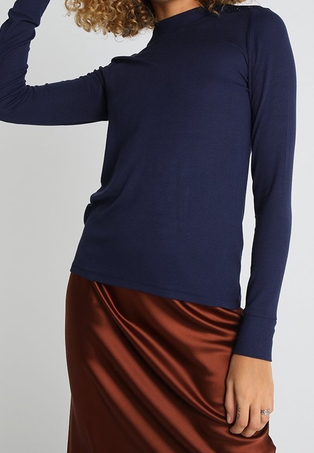 Top a maniche lunghe color navy realizzato in tessuto morbido, con un design aderente e scollatura rotonda. Abbinato a una gonna in satin marrone lucido.