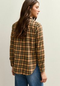 Bruin-zwart geruit overhemd met lange mouwen, iets losser vallend, een enkele borstzak en een afgeronde zoom, gemaakt van zachte stof.