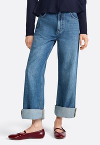 Light blue denim jeans with a loose fit, featuring rolled cuffs and subtle fading. Paired with glossy burgundy flats.