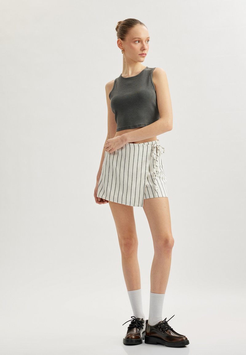 Grå ribbet crop top parret med en hvid nederdel med sorte lodrette striber og en knyte-detalje, båret med sorte sko og grå sokker.